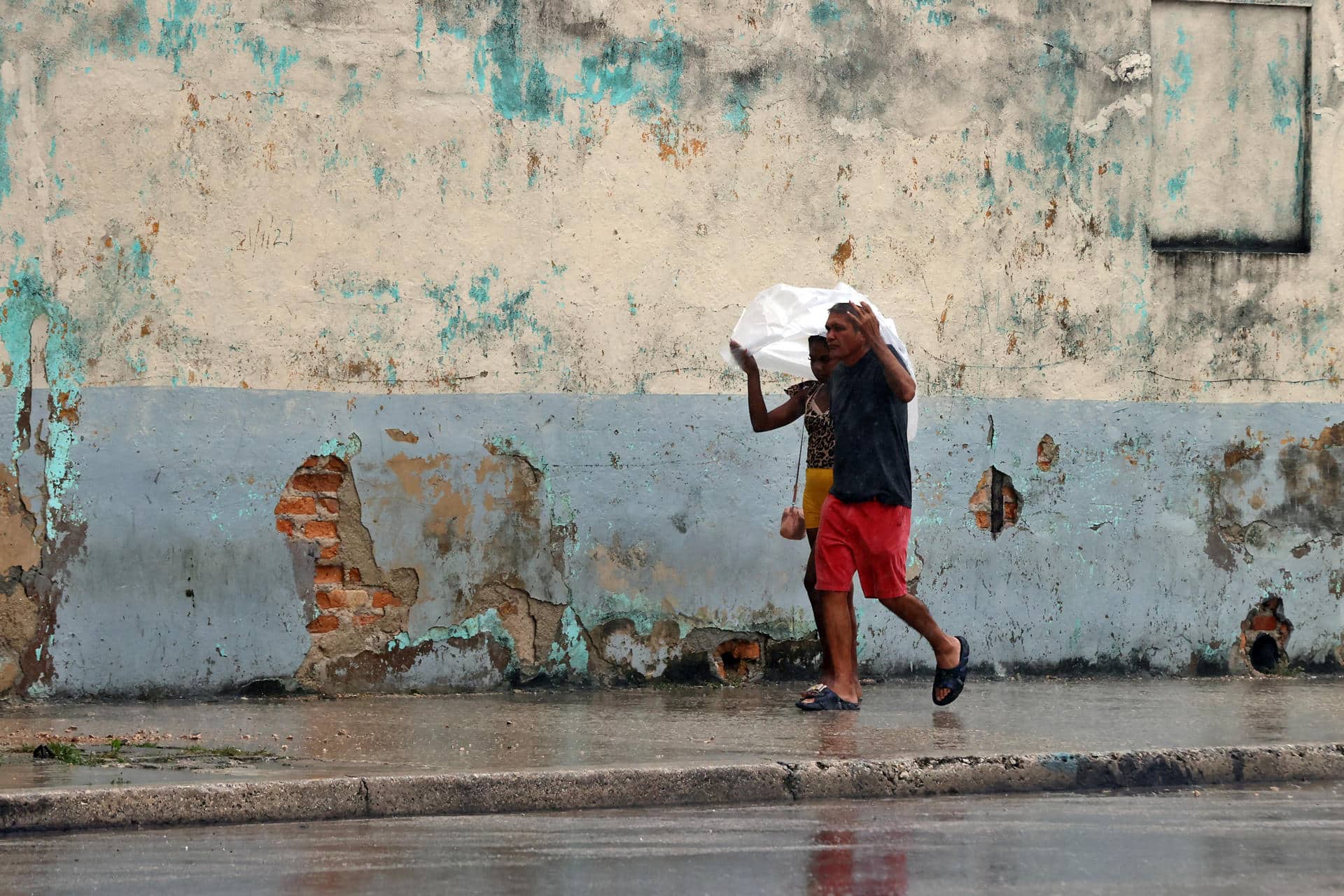 Personas se protegen de la lluvia y los fuertes vientos debido al paso del huracán Rafael en La Habana (Cuba). EFE/ Ernesto Mastrascusa