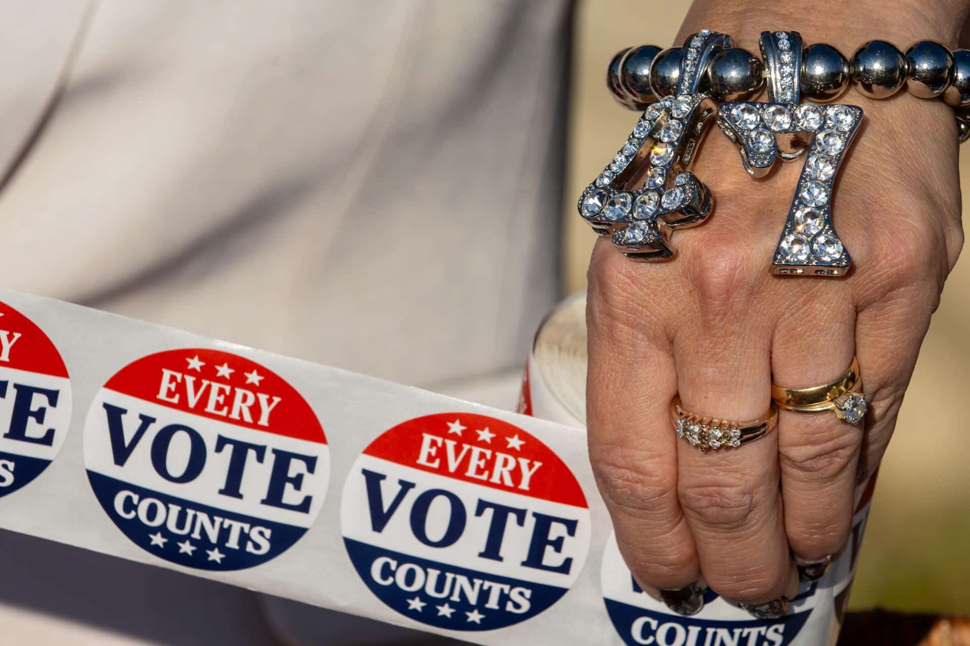 Un partidario de Trump que lleva una pulsera con la leyenda "47" sostiene pegatinas con la leyenda "Cada voto cuenta" fuera de un centro de votación el día de las elecciones en Filadelfia, Pensilvania, el 5 de noviembre de 2024.EFE/EPA/David Muse