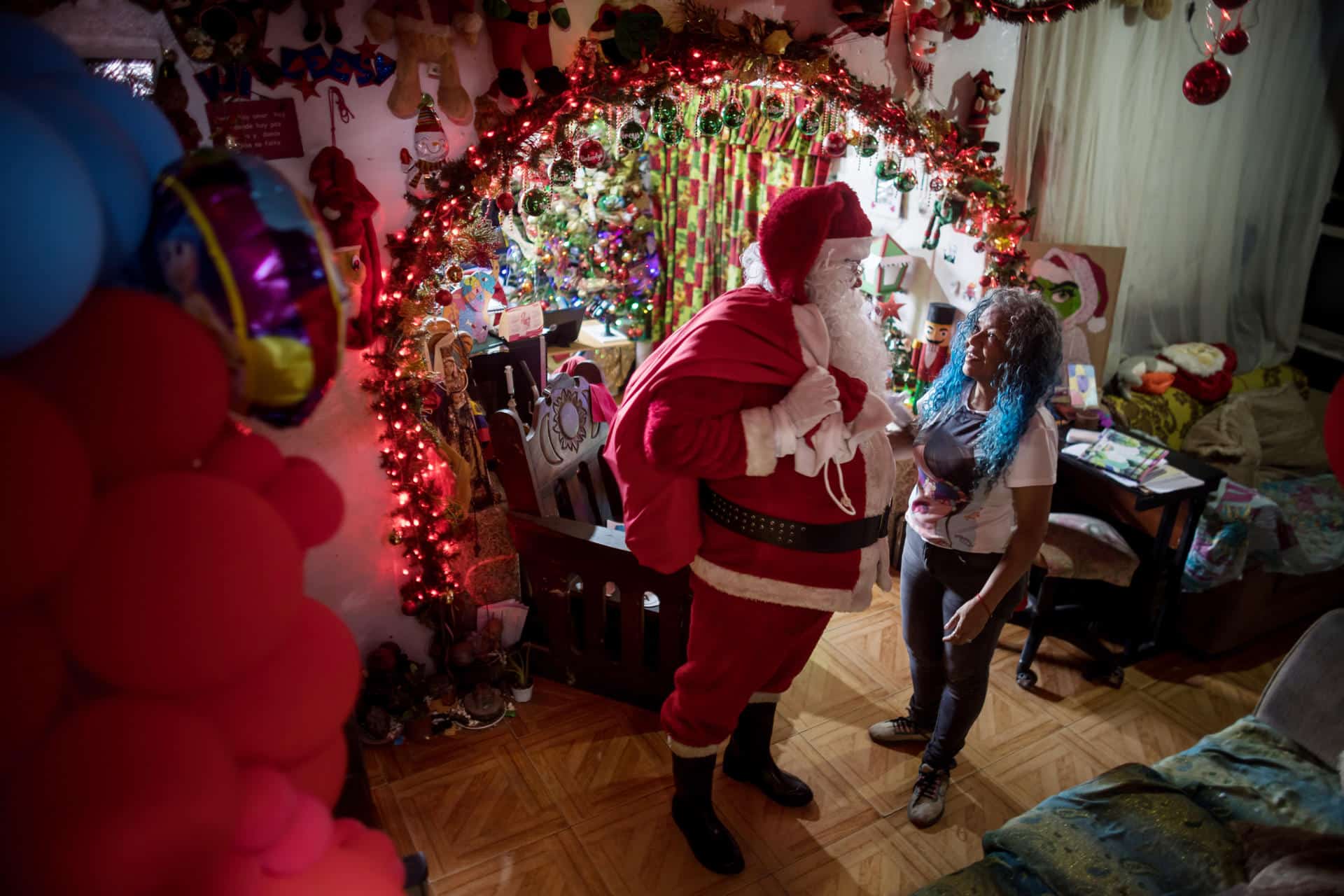 Un hombre vestido como Papá Noel saluda a una mujer en una casa este sábado, en Caracas (Venezuela). EFE/ Miguel Gutiérrez