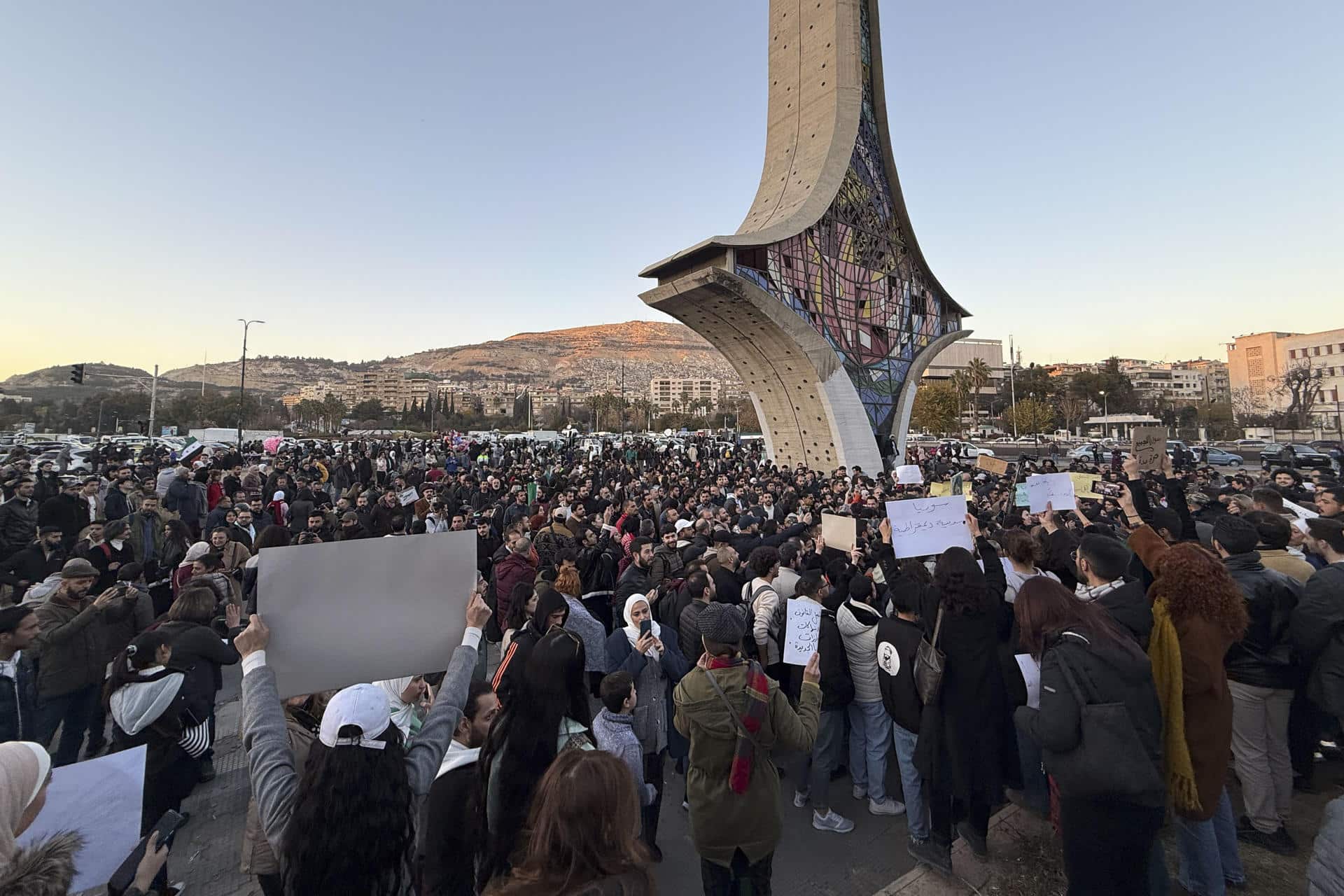 Centenares de personas se concentraron este jueves ante el monumento de la Espada Damascena, en la céntrica plaza de los Omeyas, en Damasco, portando pancartas y cantando lemas en defensa de una sociedad civil fuerte y diversa en un país laico que respete todas las sensibilidades religiosas. Ese es el mensaje compartido que han lanzado los manifestantes al nuevo Gobierno interino de Siria, que se estableció tras el derrocamiento del régimen del depuesto presidente Bachar al Asad, que se culminó el pasado 8 de diciembre con la caída de la capital en manos de la coalición islamista liderada por el Organismo de Liberación del Levante (Hayat Tahrir al Sham, o HTS en árabe). EFE/ Yahya Nemah