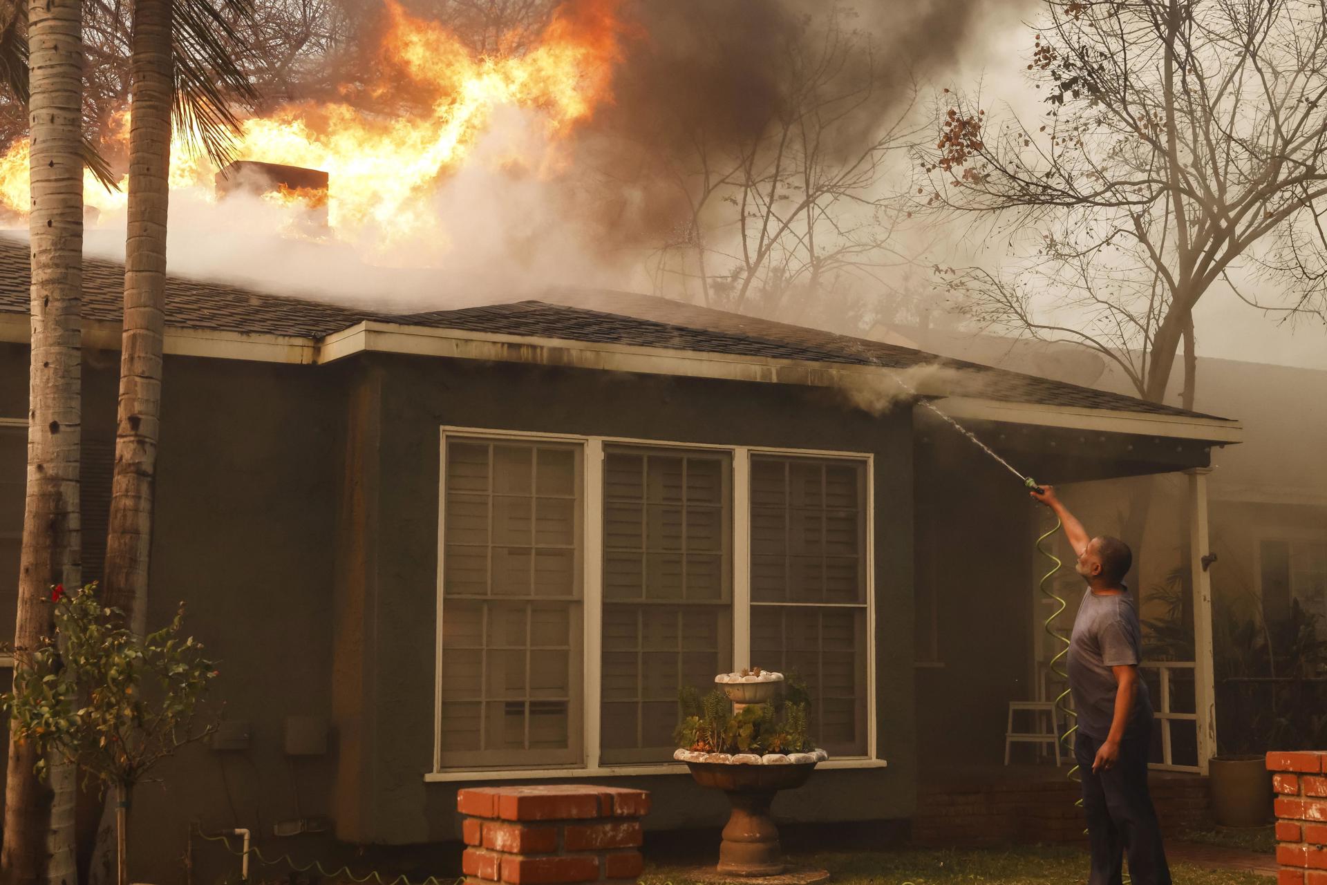 Un hombre utiliza una manguera de jardín para apagar las llamas en el tejado de una casa que arde como consecuencia del incendio forestal Eaton en Altadena, California (EE.UU.). EFE/CAROLINE BREHMAN