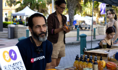 Fotografía del 11 de enero de 2025 de José Crespo posando junto a carteles de aceptación de bitcoin como forma de pago, en el Mercado Agrícola del Viejo San Juan (Puerto Rico). EFE/ Esther Alaejos