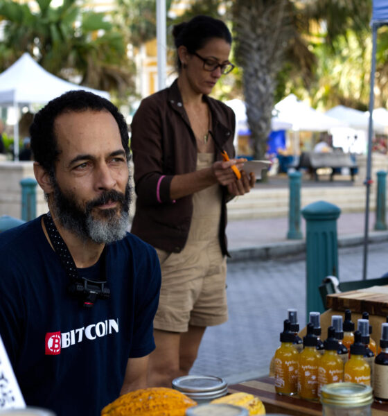 Fotografía del 11 de enero de 2025 de José Crespo posando junto a carteles de aceptación de bitcoin como forma de pago, en el Mercado Agrícola del Viejo San Juan (Puerto Rico). EFE/ Esther Alaejos