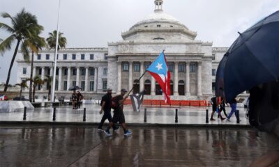 Unas personas con banderas nacionales caminan frente al Capitolio, de la Cámara de Representantes y el Senado, en San Juan (Puerto Rico). Archivo. EFE/Thais Llorca