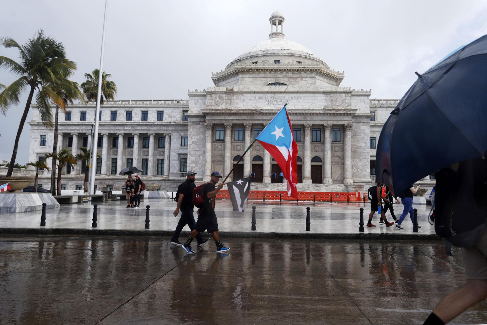 Unas personas con banderas nacionales caminan frente al Capitolio, de la Cámara de Representantes y el Senado, en San Juan (Puerto Rico). Archivo. EFE/Thais Llorca