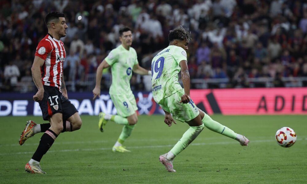 El delantero del FC Barcelona, Lamine Yamal (d), golpea el balón ante el defensa del Athletic Club, Yuri Berchiche, en la jugada que ha significado el segundo gol del equipo barcelonista durante el partido de semifinales de la Supercopa de España de fútbol que FC Barcelona y Athletic Club disputaron en el estadio Rey Abdullah de Yeda, en Arabia Saudí. EFE/Alberto Estévez.