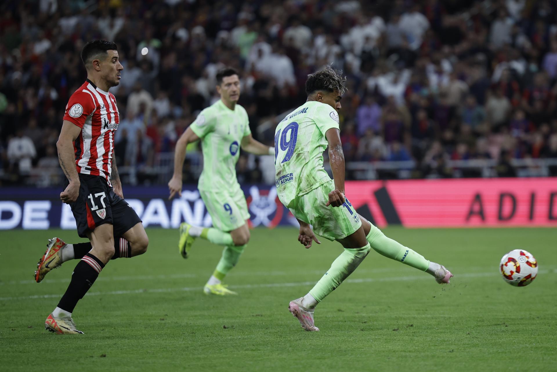 El delantero del FC Barcelona, Lamine Yamal (d), golpea el balón ante el defensa del Athletic Club, Yuri Berchiche, en la jugada que ha significado el segundo gol del equipo barcelonista durante el partido de semifinales de la Supercopa de España de fútbol que FC Barcelona y Athletic Club disputaron en el estadio Rey Abdullah de Yeda, en Arabia Saudí. EFE/Alberto Estévez.