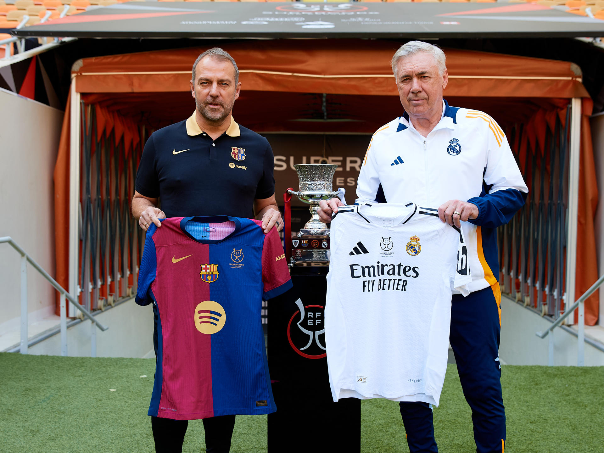 Los entrenadores del Real Madrid CF y el FC Barcelona, Carlo Ancelotti (d) y Hansi Flick (i), respectivamente, han posado este sábado junto al trofeo en el estadio Al Jawhara de Yeda, que mañana acogerá la final de la Supercopa de España. EFE/RFEF/David Aliaga