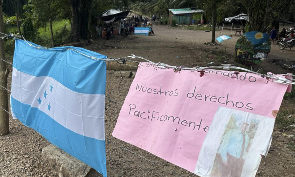 Fotografía del 12 de enero de 2025 de una bandera de Honduras y un cartel durante un plantón de campesinos en Quebrada de Arena (Honduras). EFE/ Germán Reyes