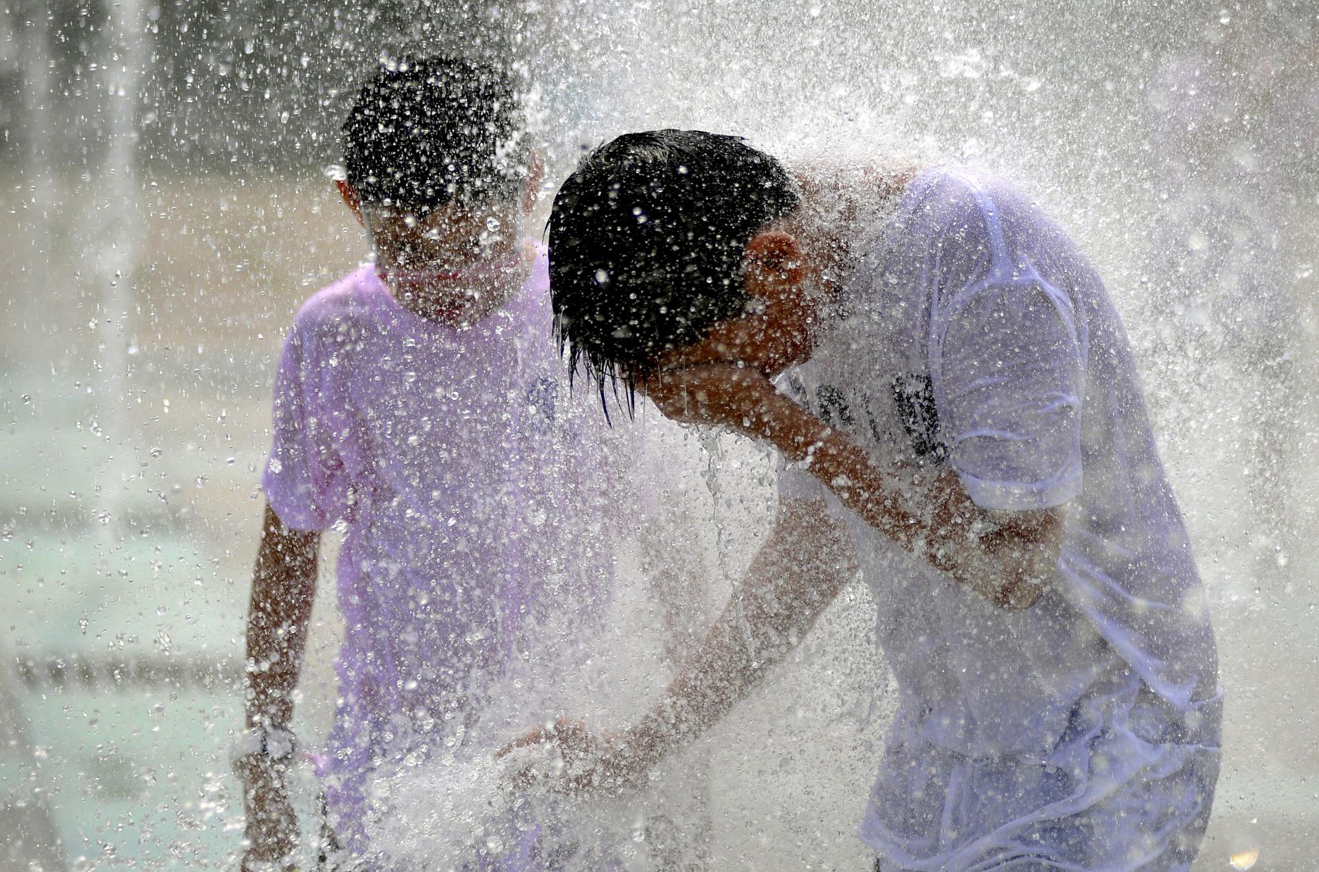 Dos jóvenes se refrescan en una fuente en Qingdao, en la provincia de Shandong (China), en una fotografía de archivo. EFE/Wu Hong