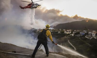 Los bomberos del condado de Los Ángeles utilizan mangueras y lanzan agua desde un helicóptero para combatir el incendio forestal de Palisades en Pacific Palisades, California, (EE.UU.). EFE/CAROLINE BREHMAN