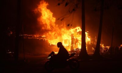 Una persona conduce su motocicleta junto a una casa en llamas durante los incendios en Palisades , California, Estados Unidos. EFE/ Allison Dinner