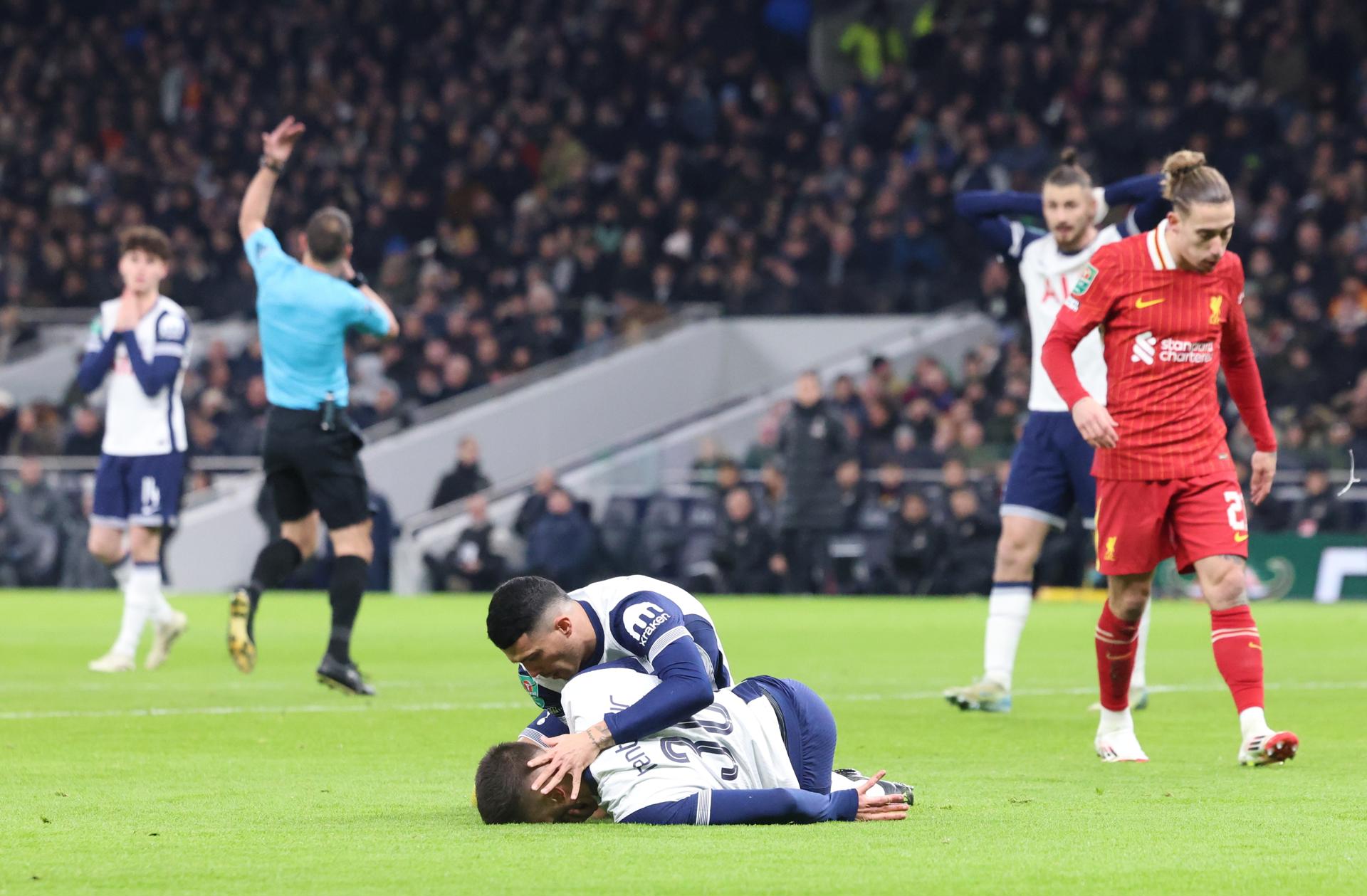 El español Pedro Porro atiende a su compañero del Tottenham, el uruguayo Rodrigo Bentancur, tendido sobre el terreno de juego durante la semifinal de Copa disputada contra el Liverpool. EFE/EPA/NEIL HALL