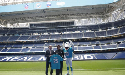 Brett Gosper, director de la NFL en Europa y Asia-Pacífico y Pri Shumate, vicepresidenta de los Miami Dolphins, en el césped del estadio Santiago Bernabéu con la mascota del equipo, durante el acto celebrado este viernes en Madrid. EFE/ Blanca Millez