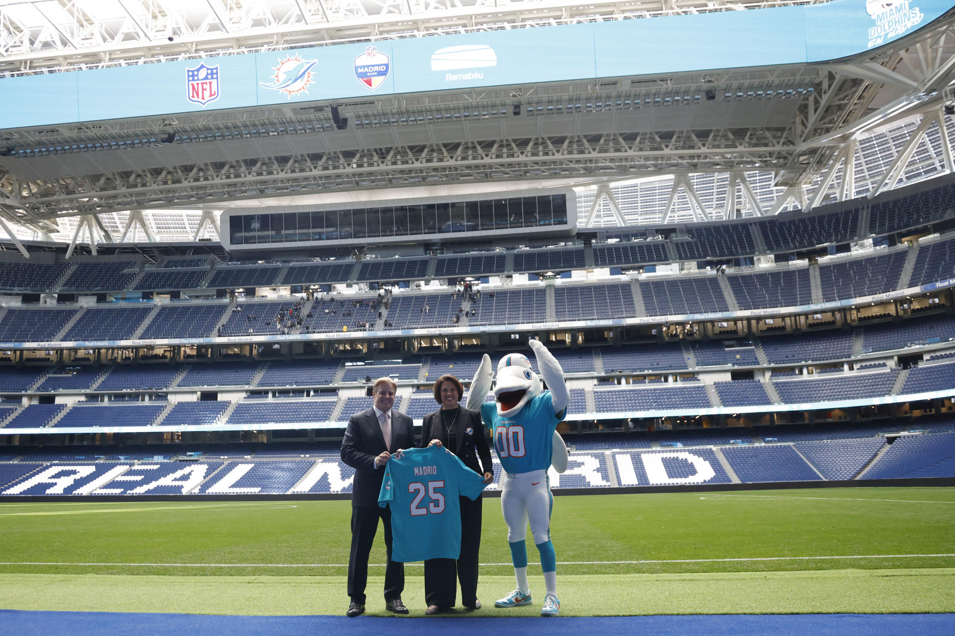 Brett Gosper, director de la NFL en Europa y Asia-Pacífico y Pri Shumate, vicepresidenta de los Miami Dolphins, en el césped del estadio Santiago Bernabéu con la mascota del equipo, durante el acto celebrado este viernes en Madrid. EFE/ Blanca Millez