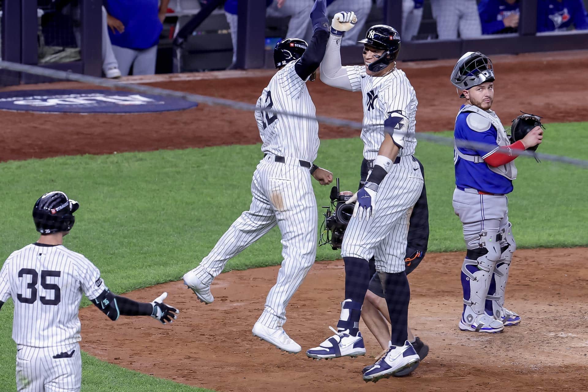 El jardinero derecho de los New York Yankees, Aaron Judge (C), celebra con el jardinero central, Trent Grisham (I), después de conectar un jonrón de tres carreras, mientras el receptor de los Toronto Blue Jays, Alejandro Kirk (D), observa en la cuarta entrada del juego 3 de la serie de playoffs de la División Americana de la MLB. EFE/EPA/SARAH YENESEL