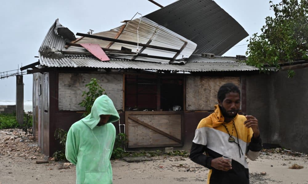 Personas pasan frente a una casa afectada por los vientos preliminares del huracán Melissa este lunes, en la playa pesquera de Hellshire, en Portmore (Jamaica). EFE/Rudolph Brown