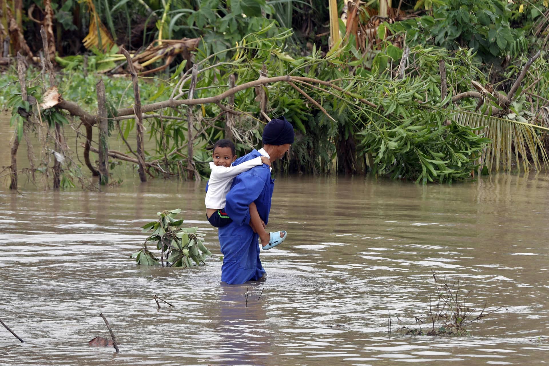 Un hombre fue captado este miércoles, 29 de octubre, al cruzar un río crecido mientras carga a un niño a sus espaldas, tras el paso del huracán Melissa, en el poblado de Guama, en Santiago de Cuba (Cuba). EFE/Ernesto Mastrascusa