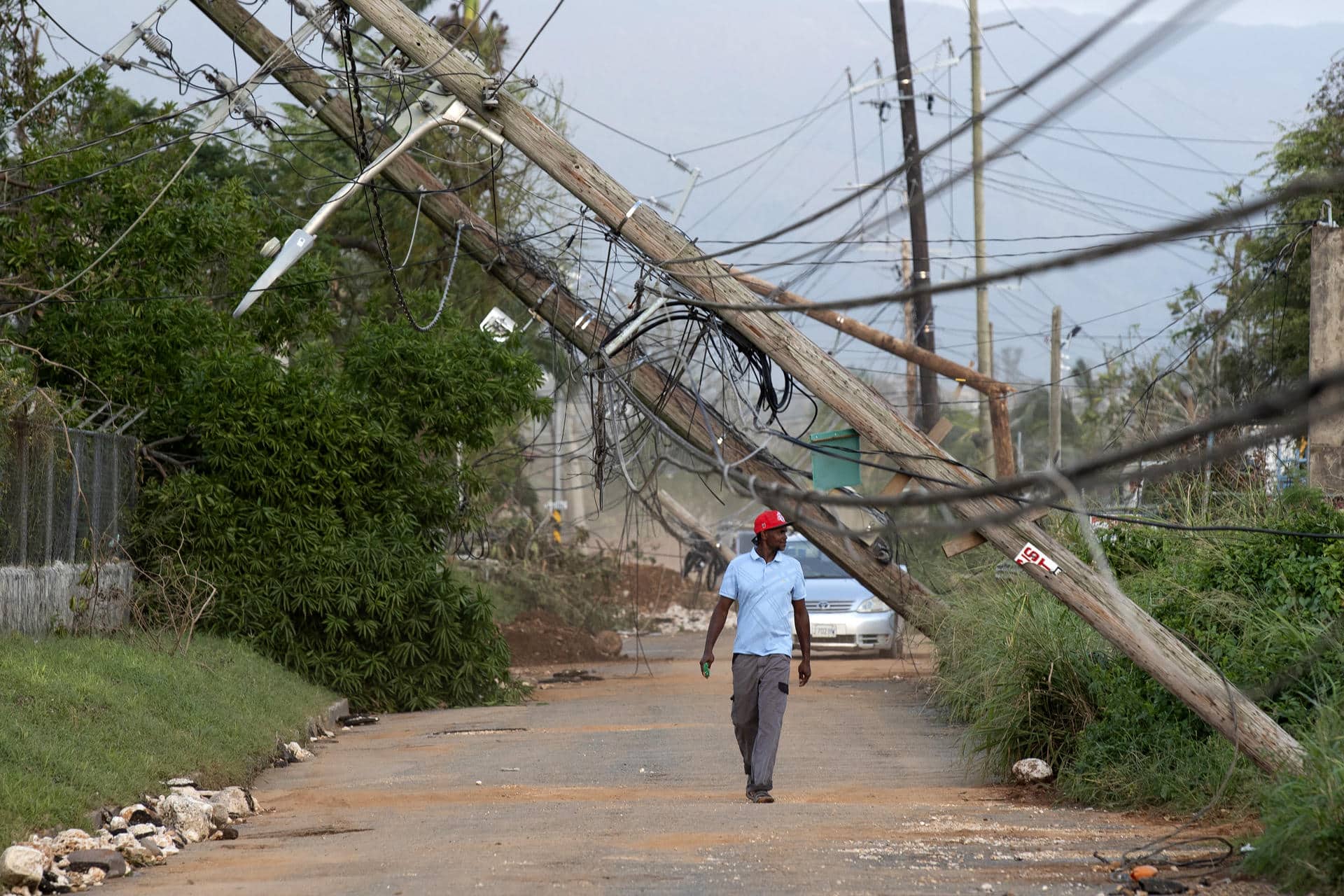 Una hombre fue captado este 30 de octubre al caminar bajo varios postes del tendido eléctrico derribados por el huracán Melissa en Santa Cruz (Jamaica). EFE/Orlando Barría