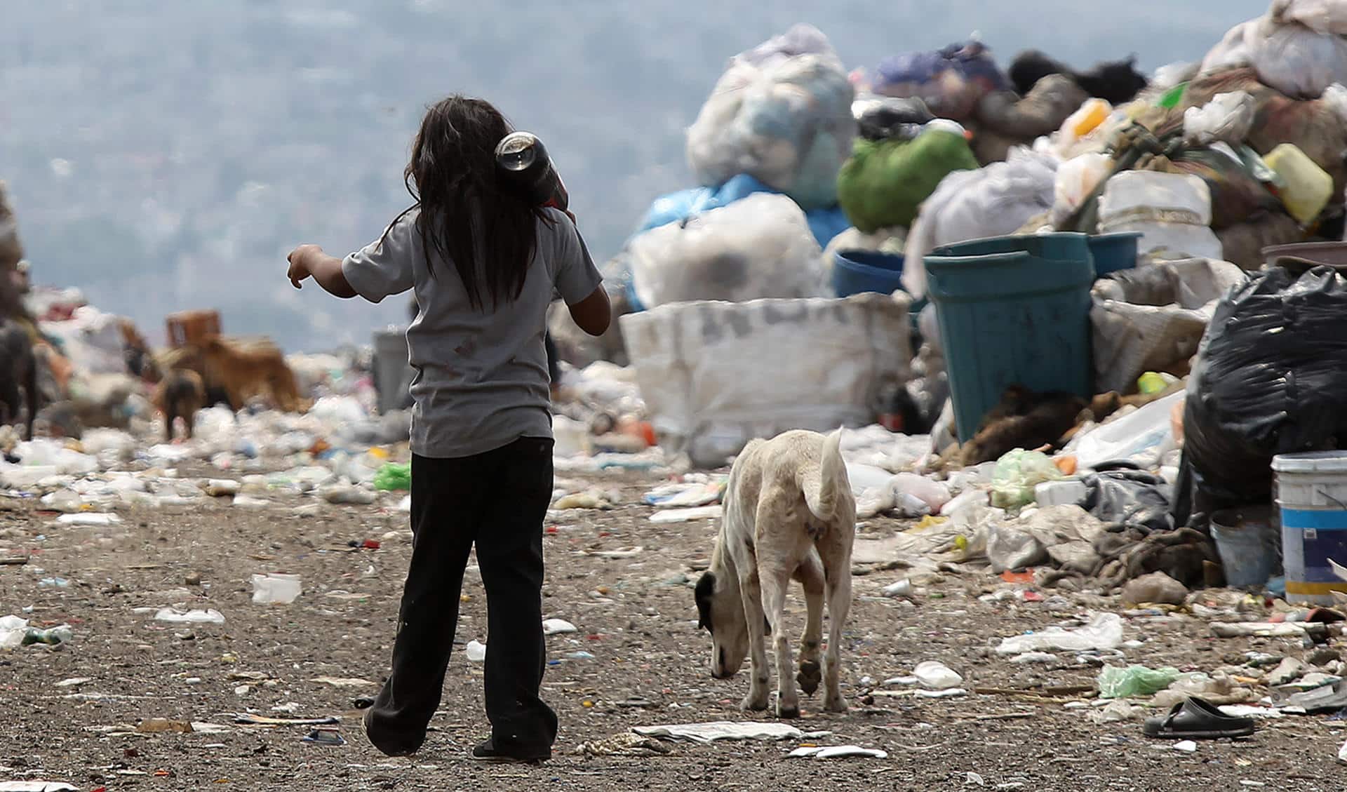 Fotografía de archivo de un niño con su perro caminando rumbo a su casa entre montañas de basura en el vertedero municipal del Bordo de Xochiaca, en Ciudad Nezahualcoyotl (México). EFE/Alex Cruz