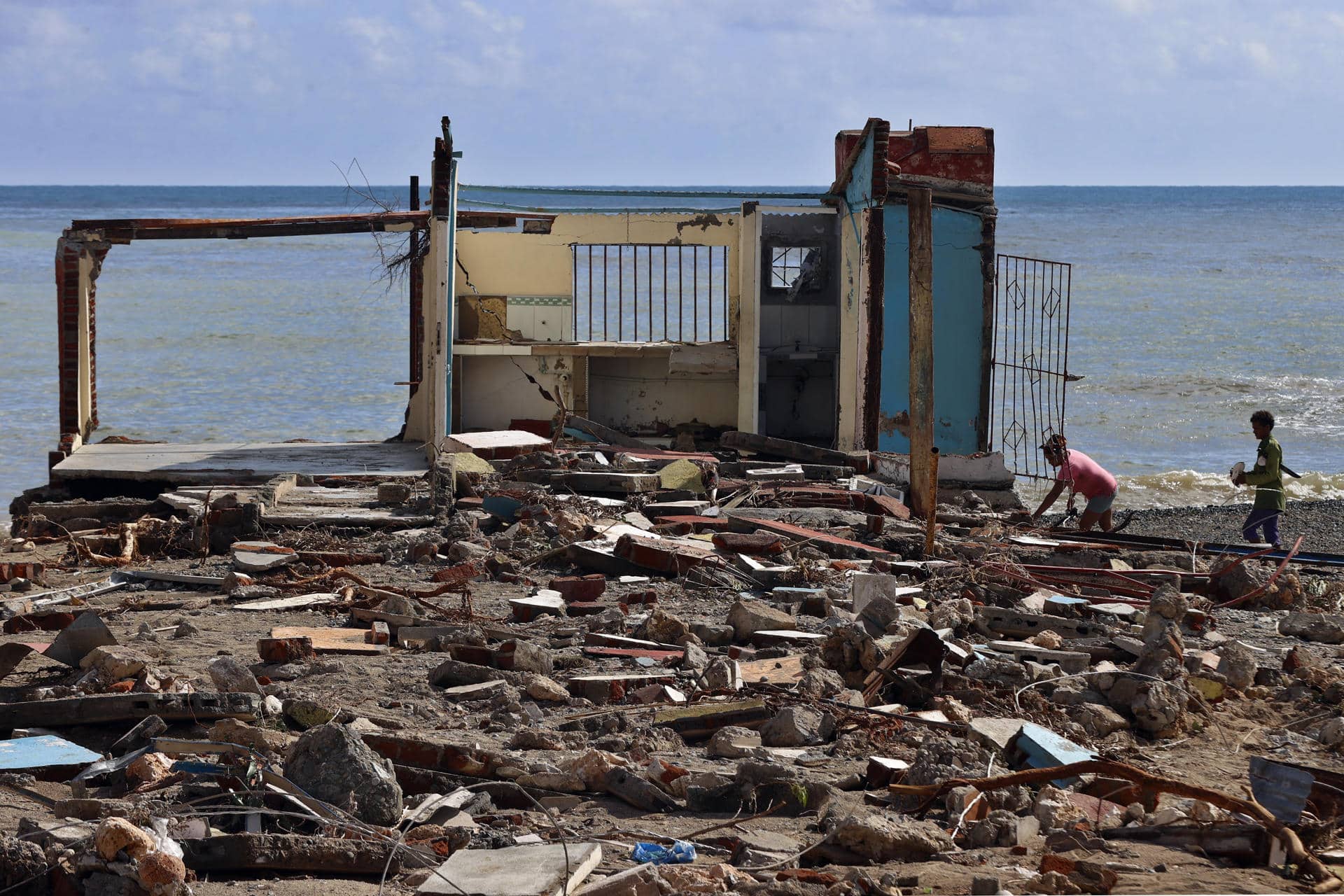 Personas caminan frente a una casa destruida, este jueves en el poblado de Guamá, Santiago de Cuba (Cuba). EFE/ Ernesto Mastrascusa