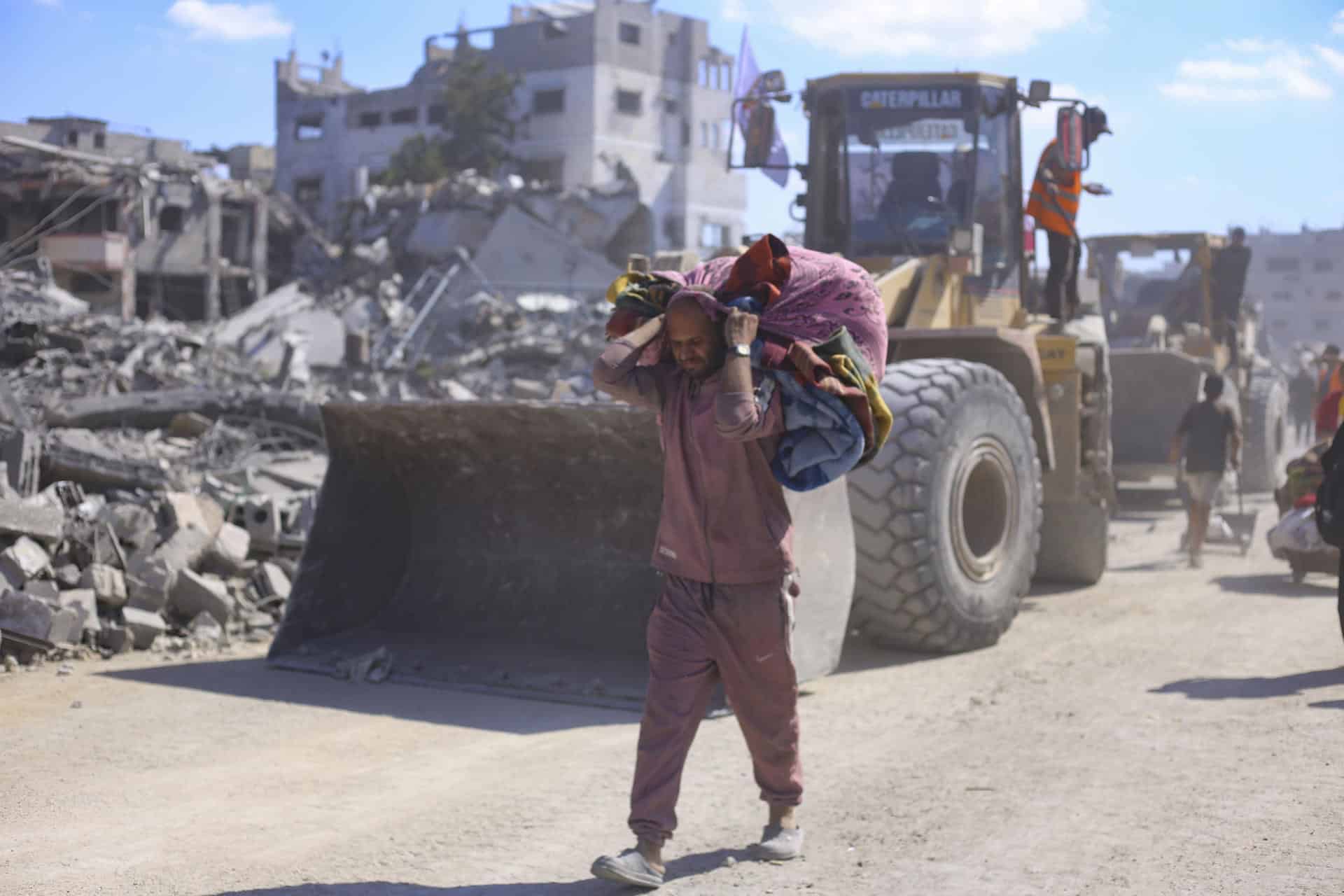 Un hombre con un hatillo con sus pertenencias pasa ante varias excavadoras del Ayuntamiento de la ciudad de Gaza que comienza este martes las operaciones de remoción de escombros y apertura de las calles principales de la capital gazatí para despejarlas y prepararlas para su uso, tras dos años de bombardeos. EFE/ Ahmad Awad