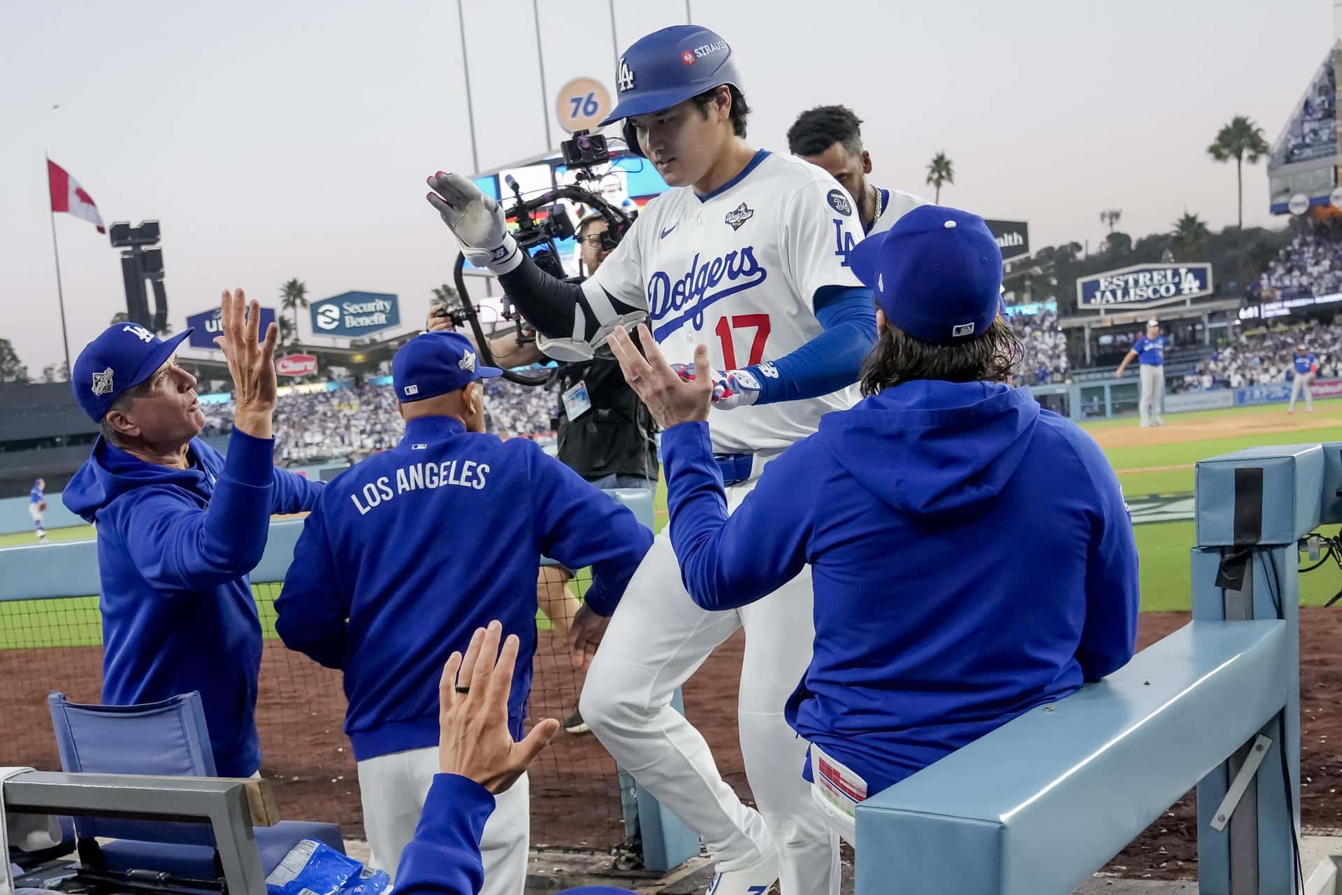 El bateador designado de los Los Angeles Dodgers, Shohei Ohtani (c), es recibido en el dugout después de conectar un jonrón en solitario contra los Azulejos de Toronto durante la tercera entrada del tercer juego de la Serie Mundial de la MLB. EFE/EPA/ALLISON DINNER