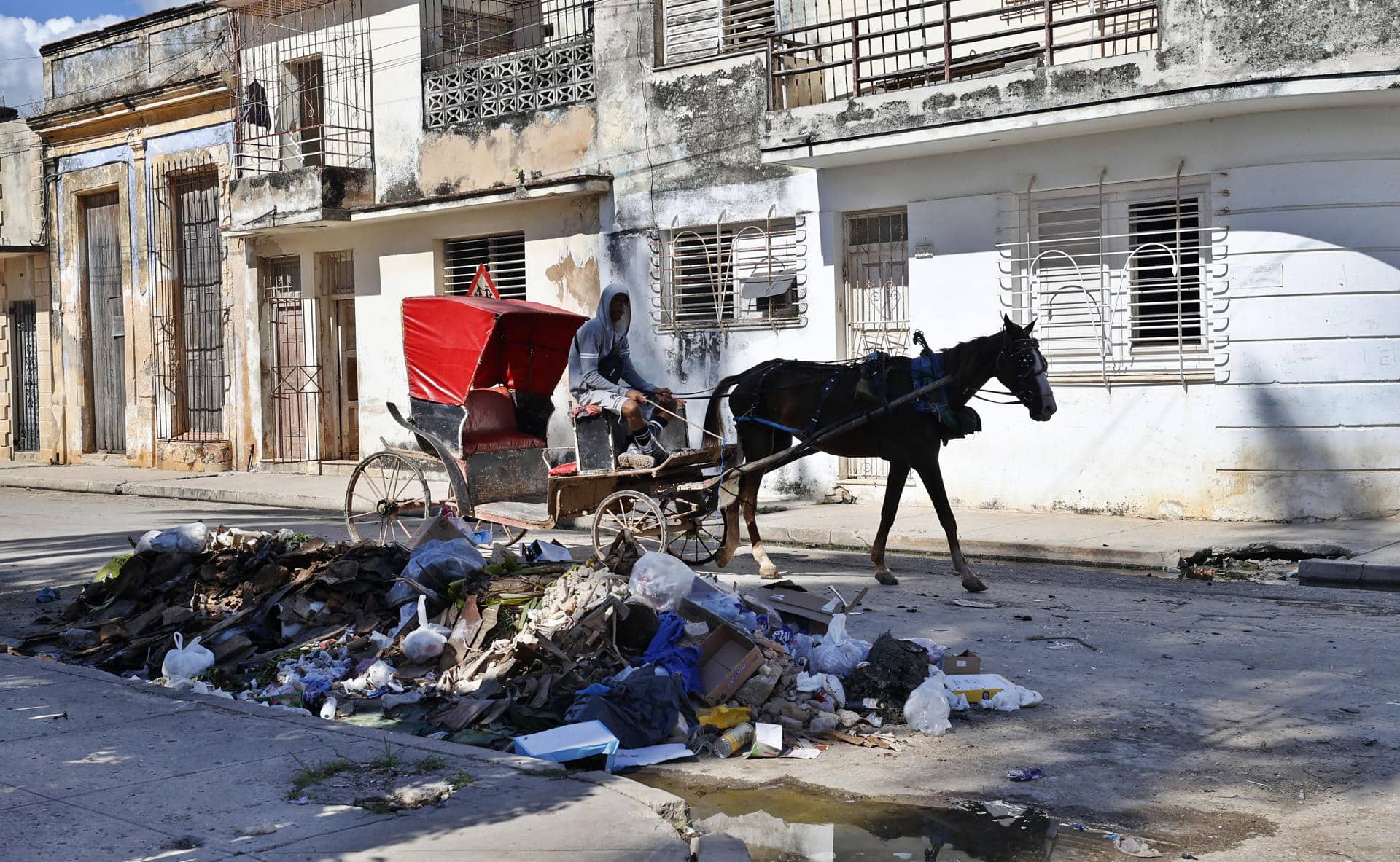 Una persona se transporta en una carreta frente a escombros y basura este viernes, en Cárdenas (Cuba). EFE/ Ernesto Mastrascusa