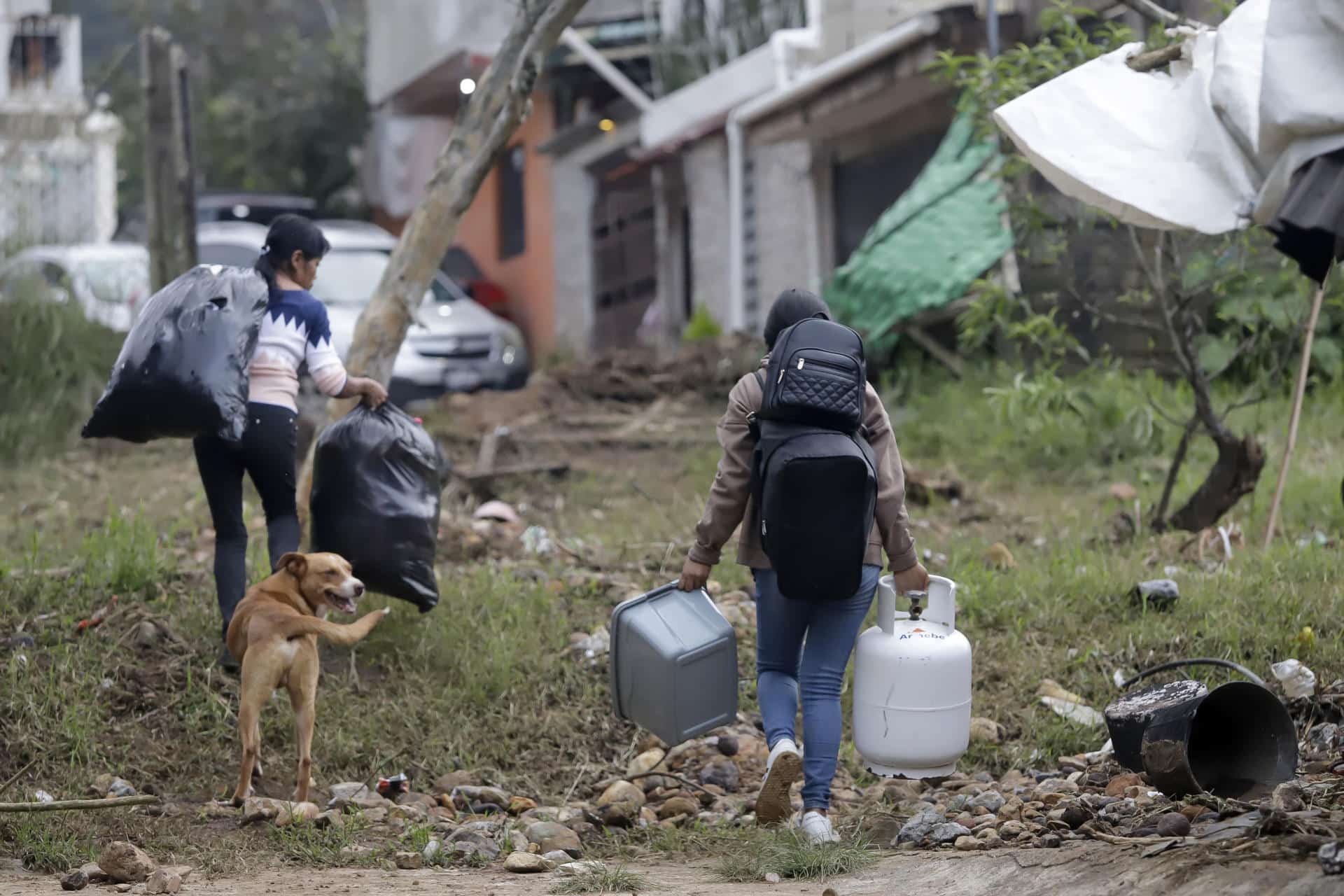 Personas caminan con sus pertenencias en una zona afectada por las fuertes lluvias en Huauchinango (México). EFE/ Hilda Ríos