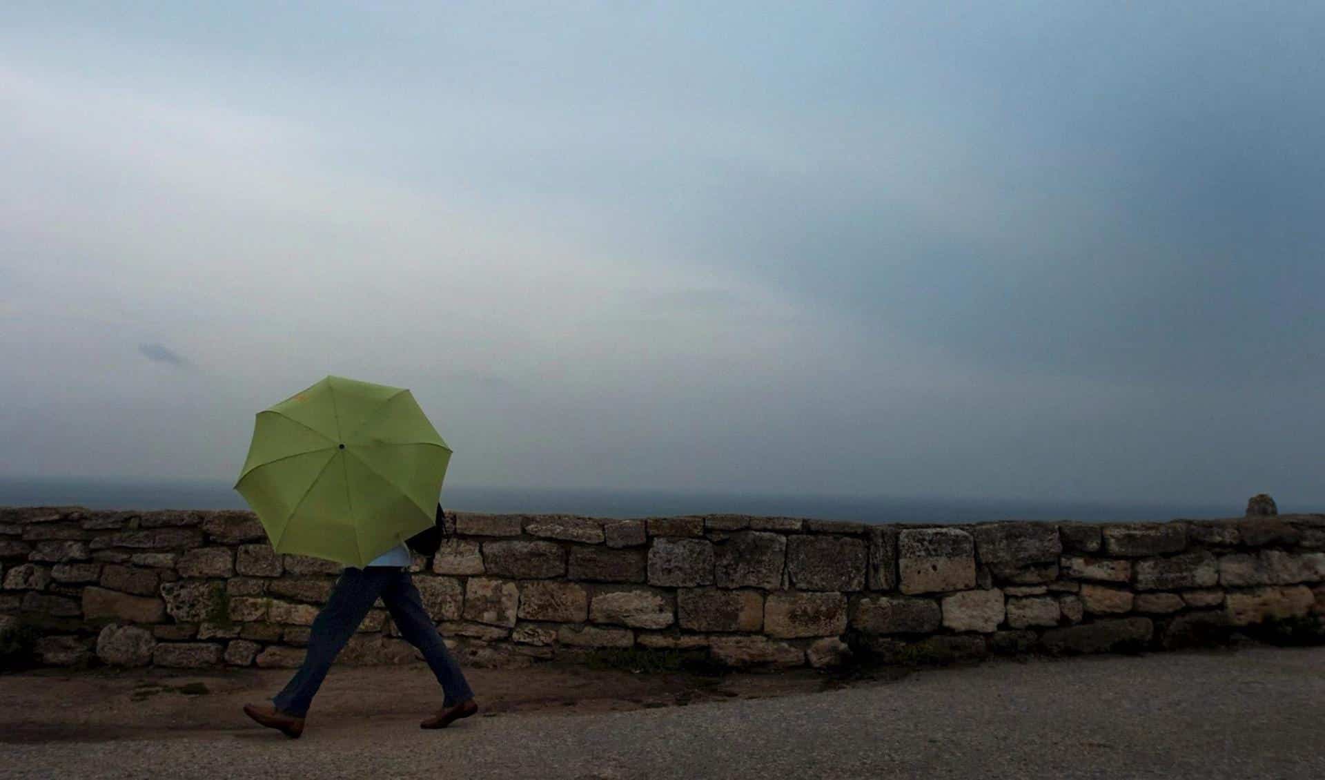 Una mujer camina con un paraguas durante una tormenta en Kaliakra, a unos 500 kilómetros de Sofía (Bulgaria). EFE/Vassil Donev