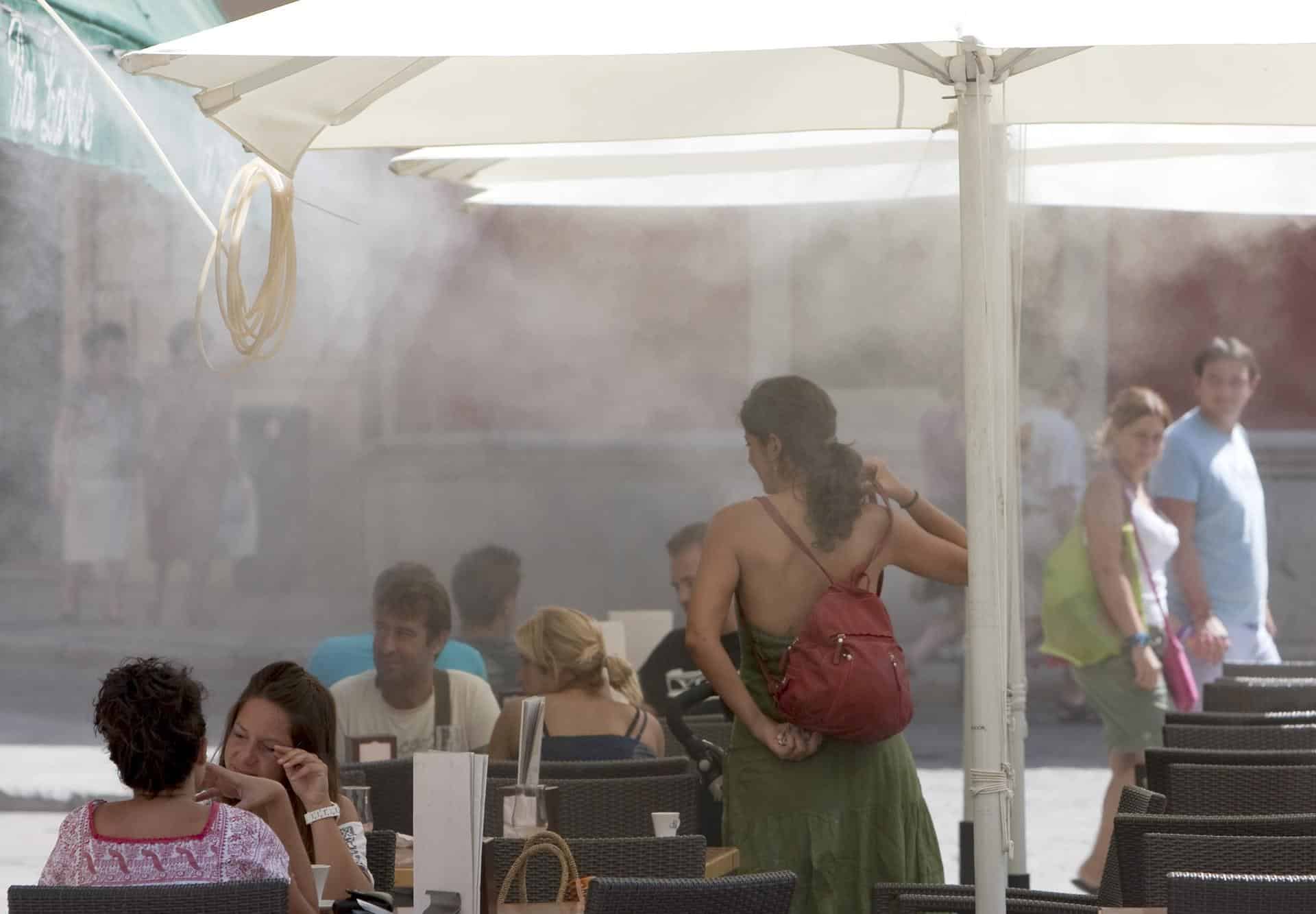 Unos turistas se refrescan en una terraza gracias a unas sombrillas equipadas con difusores de agua en la provincia de Sevilla, en una imagen de archivo. EFE/Julio Muñoz