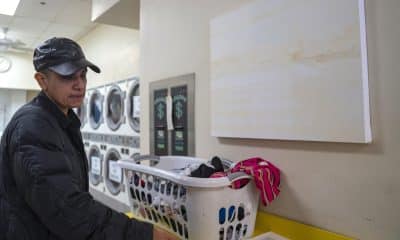 La encargada del proyecto artístico Desnivel, María de Victoria, lava su ropa frente a una obra colgada de la artista Gloria Maximo en una lavandería este viernes, en Nueva York (Estados Unidos). EFE/ Ángel Colmenares