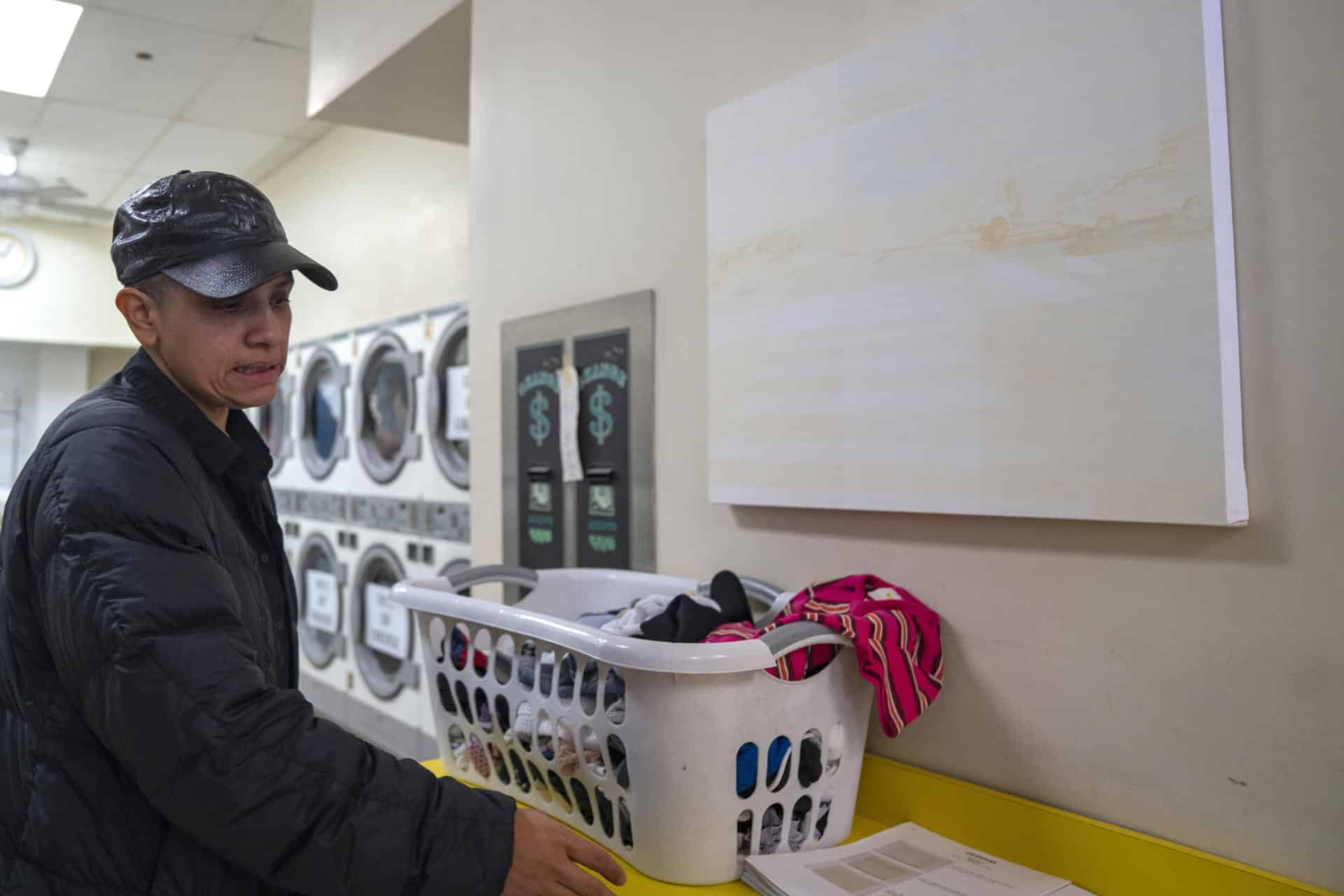 La encargada del proyecto artístico Desnivel, María de Victoria, lava su ropa frente a una obra colgada de la artista Gloria Maximo en una lavandería este viernes, en Nueva York (Estados Unidos). EFE/ Ángel Colmenares