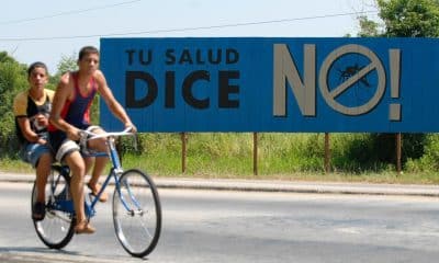 Fotografía de archivo de un par de jóvenes sobre una bicicleta al pasar frente a un cartel de campaña contra el Dengue, en Alamar (Cuba). EFE/Orlando Barría