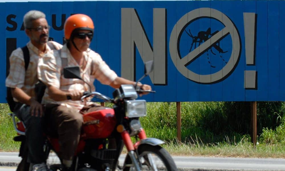 Fotografía de archivo en la que se captó a un par de ciudadanos al pasar en un motocicleta frente a un cartel de una campaña contra el dengue en Alamar (Cuba). EFE/Orlando Barría