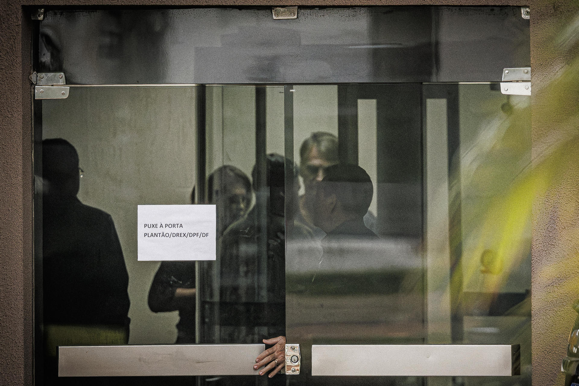 Fotografía que muestra al expresidente de Brasil Jair Bolsonaro (2-d) detrás de una puerta de vidrio este domingo, en la Superintendencia de la Policía Federal en Brasilia (Brasil). EFE/ Isaac Fontana