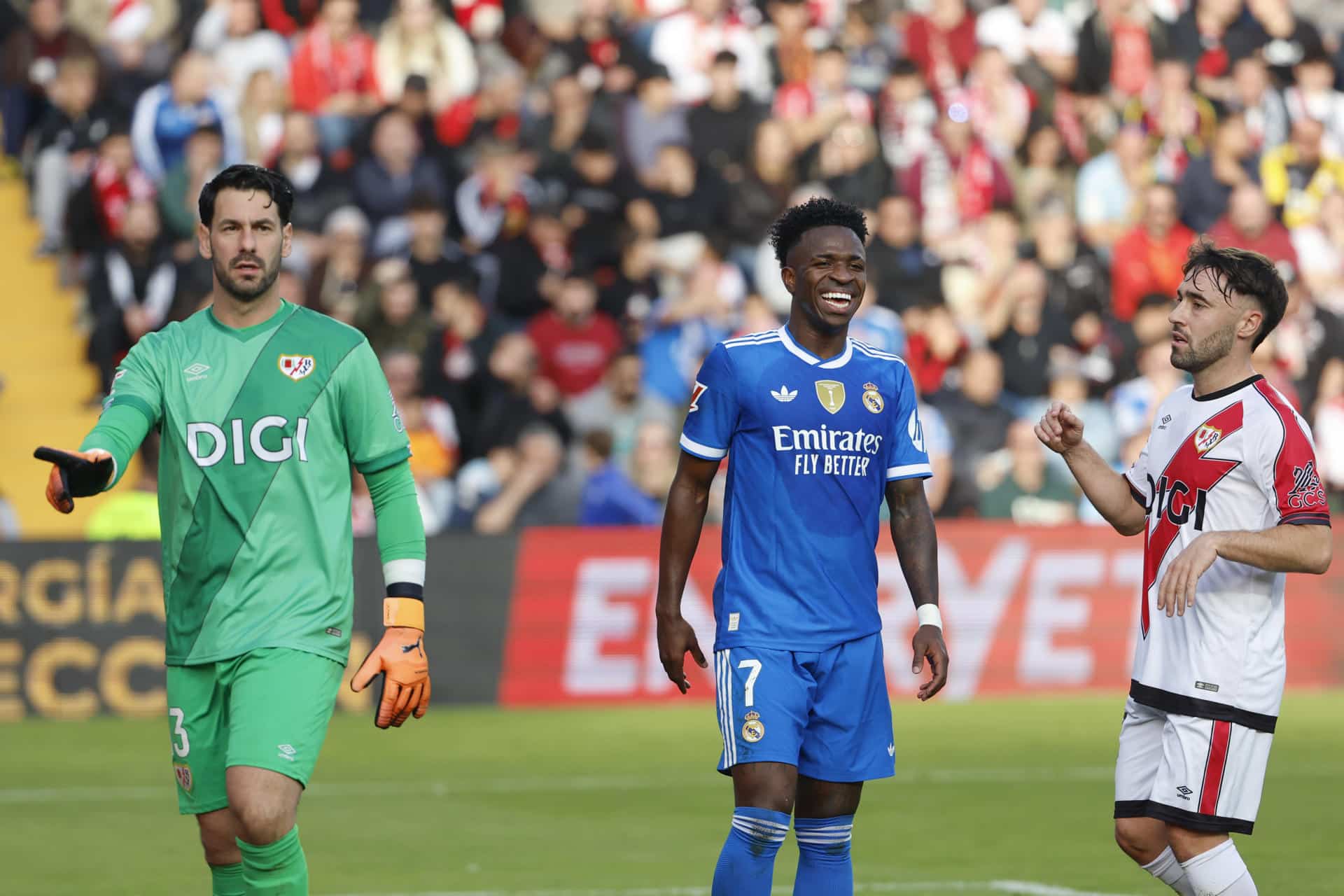 El delantero del Real Madrid Vinicius Jr (c) sonríe junto a Augusto Batalla (i) y Unai López (d), del Rayo Vallecano, durante el partido de la jornada 12 de LaLiga EA Sports que Rayo Vallecano y Real Madrid disputan este domingo en el Estadio de Vallecas, en la capital española. EFE/Mariscal