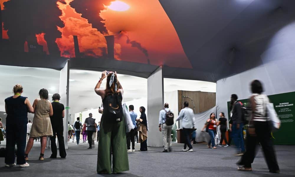 Personas caminan frente a una proyección de imágenes de desastres naturales creada por la ONG Greenpeace este viernes, en el Centro de Convenciones Hangar en Belém (Brasil). EFE/ Andre Borges