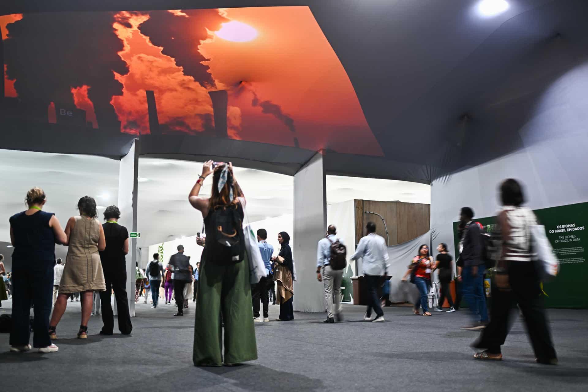 Personas caminan frente a una proyección de imágenes de desastres naturales creada por la ONG Greenpeace este viernes, en el Centro de Convenciones Hangar en Belém (Brasil). EFE/ Andre Borges