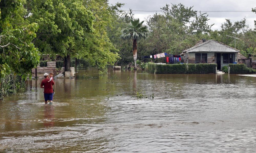 Una persona fue captada el pasado 31 de octubre al caminar con un niño en su brazos, frente a una casa inundada por la crecida de un río tras el paso de huracán Melissa, en Cauto Cristo (Cuba). EFE/Ernesto Mastrascusa