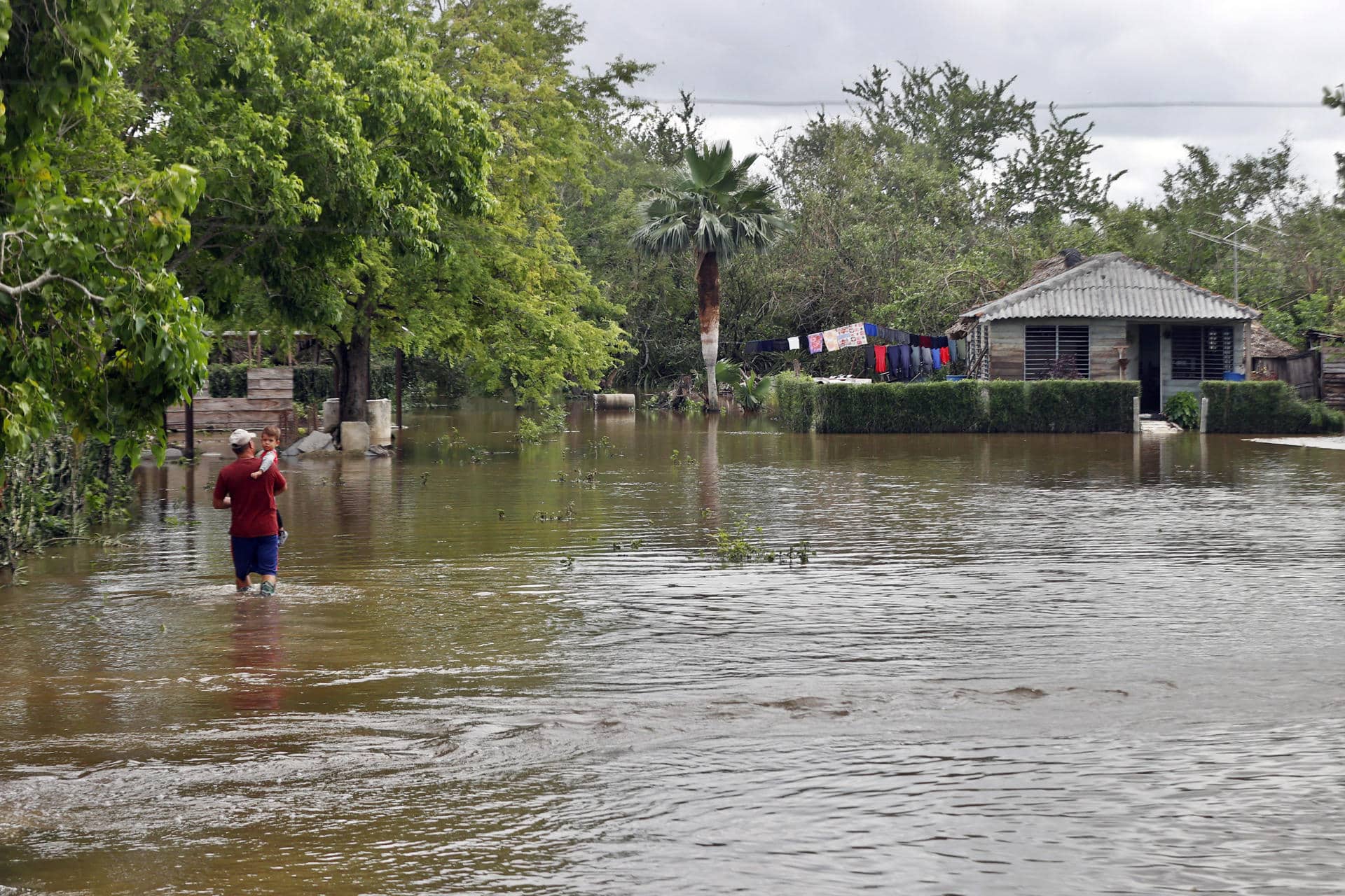 Una persona fue captada el pasado 31 de octubre al caminar con un niño en su brazos, frente a una casa inundada por la crecida de un río tras el paso de huracán Melissa, en Cauto Cristo (Cuba). EFE/Ernesto Mastrascusa