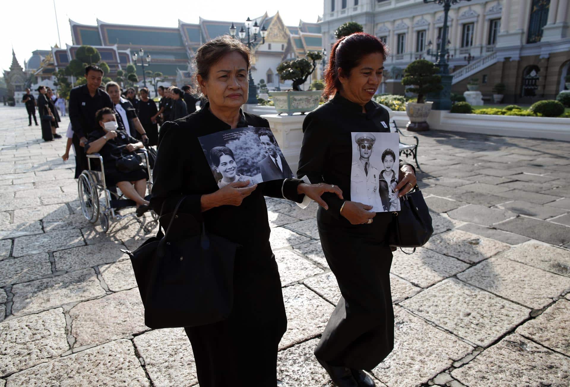 Dos mujeres tailandesas con retratos de la reina madre Sirikit y su esposo, el fallecido rey Bhumibol Adulyadej, hacen fila para rendir homenaje a la difunta en el Salón del Trono Dusit Maha Prasat dentro del Gran Palacio en Bangkok, Tailandia, el 9 de noviembre de 2025. EFE/EPA/RUNGROJ YONGRIT