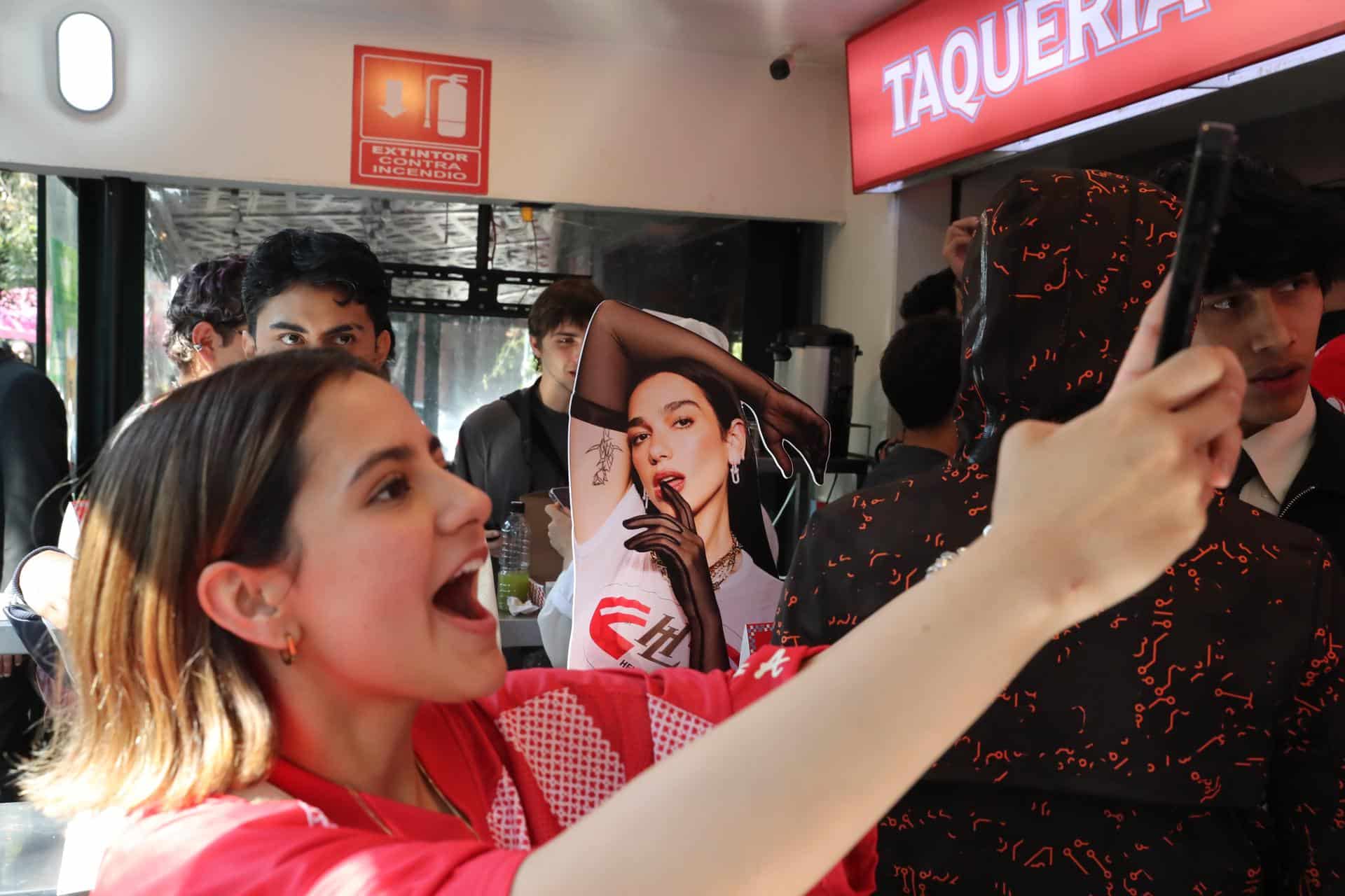Una mujer se toma una fotografía junto a un cartel de la cantante británica Dua Lipa durante la apertura de la taquería 'La Dua' este lunes, en Ciudad de México (México). EFE/ Mario Guzmán