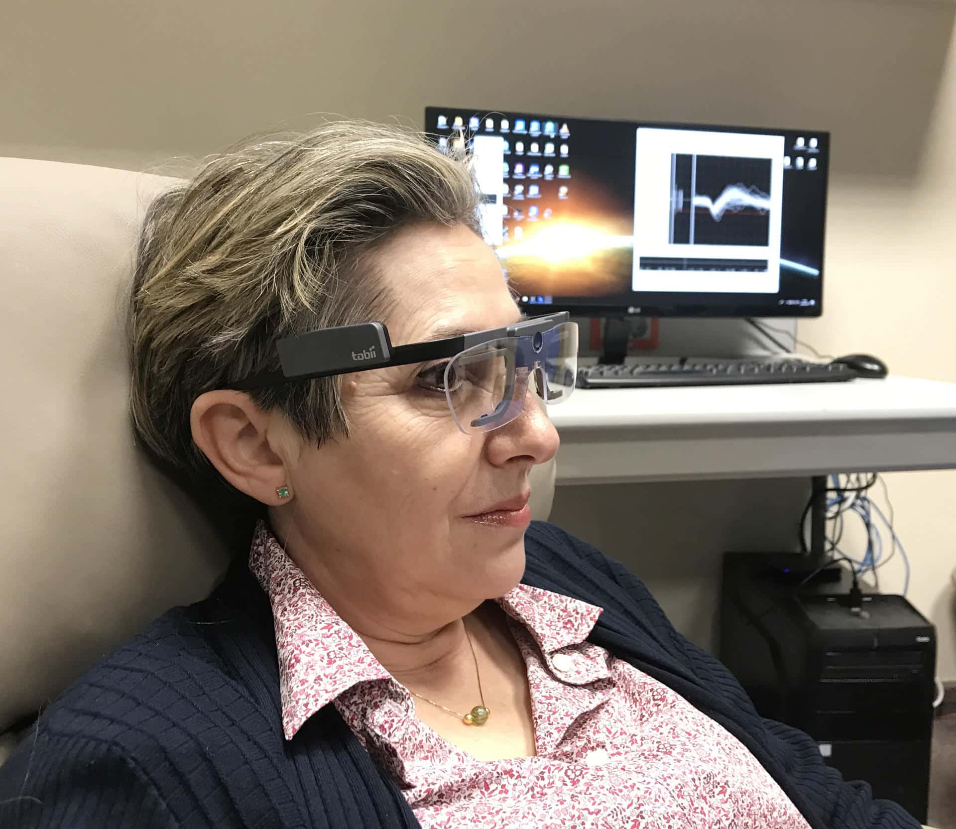 Berna_Spikes: Imagen de una paciente ciega, con una gafas para el seguimiento de su mirada y el registro de su actividad cerebral en el fondo. Cedida por el Instituto de Bioingeniería de la Universidad Miguel Hernández de Elche.
