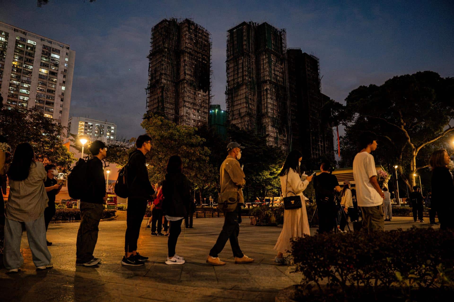 Fotografía de archivo, tomada el 29/11/2025, que muestra a personas con flores cerca del conjunto residencial incendiado Wang Fuk Court, en Hong Kong, China. EFE/EPA/LEUNG MAN HEI