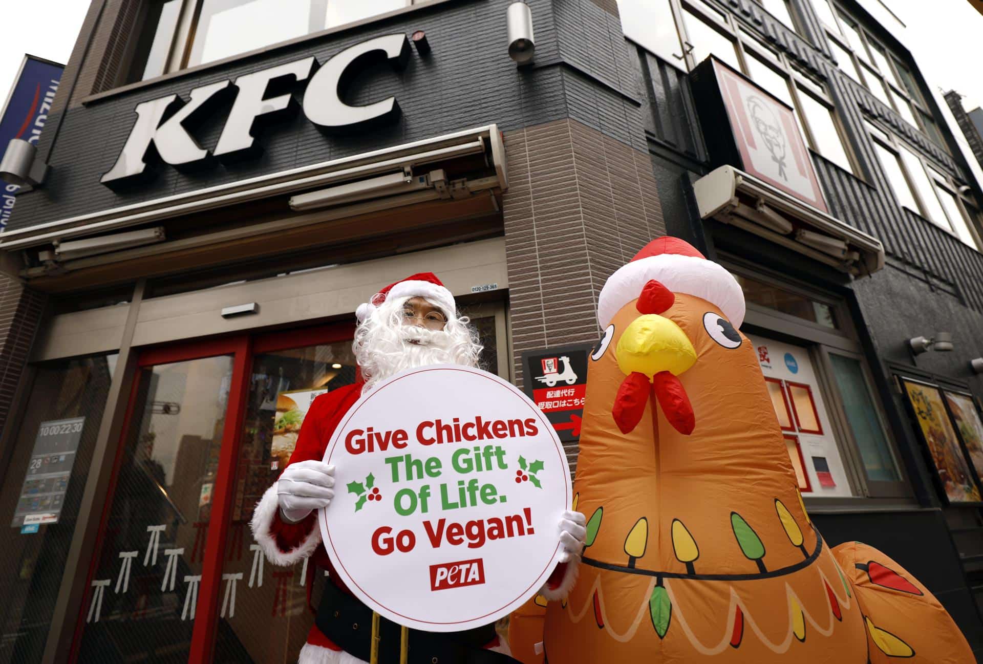 TOKYO (Japan), 03/12/2025.- Wearing a Santa Claus costume, an animal rights activist of People for the Ethical Treatment of Animals (PETA) stands next to an inflatable chicken in front of a KFC fast food restaurant in Tokyo, Japan, 03 December 2025. In a statement, PETA said it is protesting against cruelty on chickens reported at a KFC supplier in Japan. (Protestas, Japón, Tokio) EFE/EPA/FRANCK ROBICHON