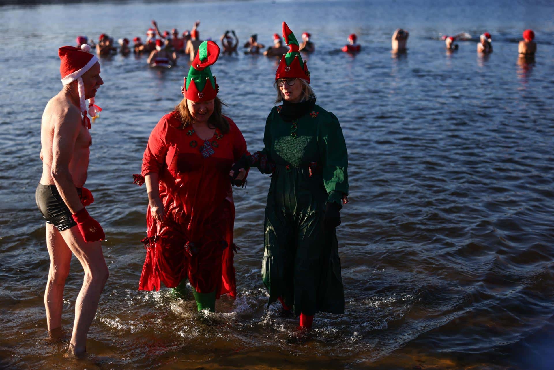 Los miembros del club 'Berlin Seals' asisten al tradicional baño navideño en el lago de Orankesee, en Berlín (Alemania), este jueves 25 de diciembre de 2025. La mayoría de ellos, vestidos con trajes de baño, trajes típicos de la temporada o, al menos, gorros de Papá Noel,se reunieron para su baño anual en las aguas del lago, a temperaturas invernales. EFE/HANNIBAL HANSCHKE