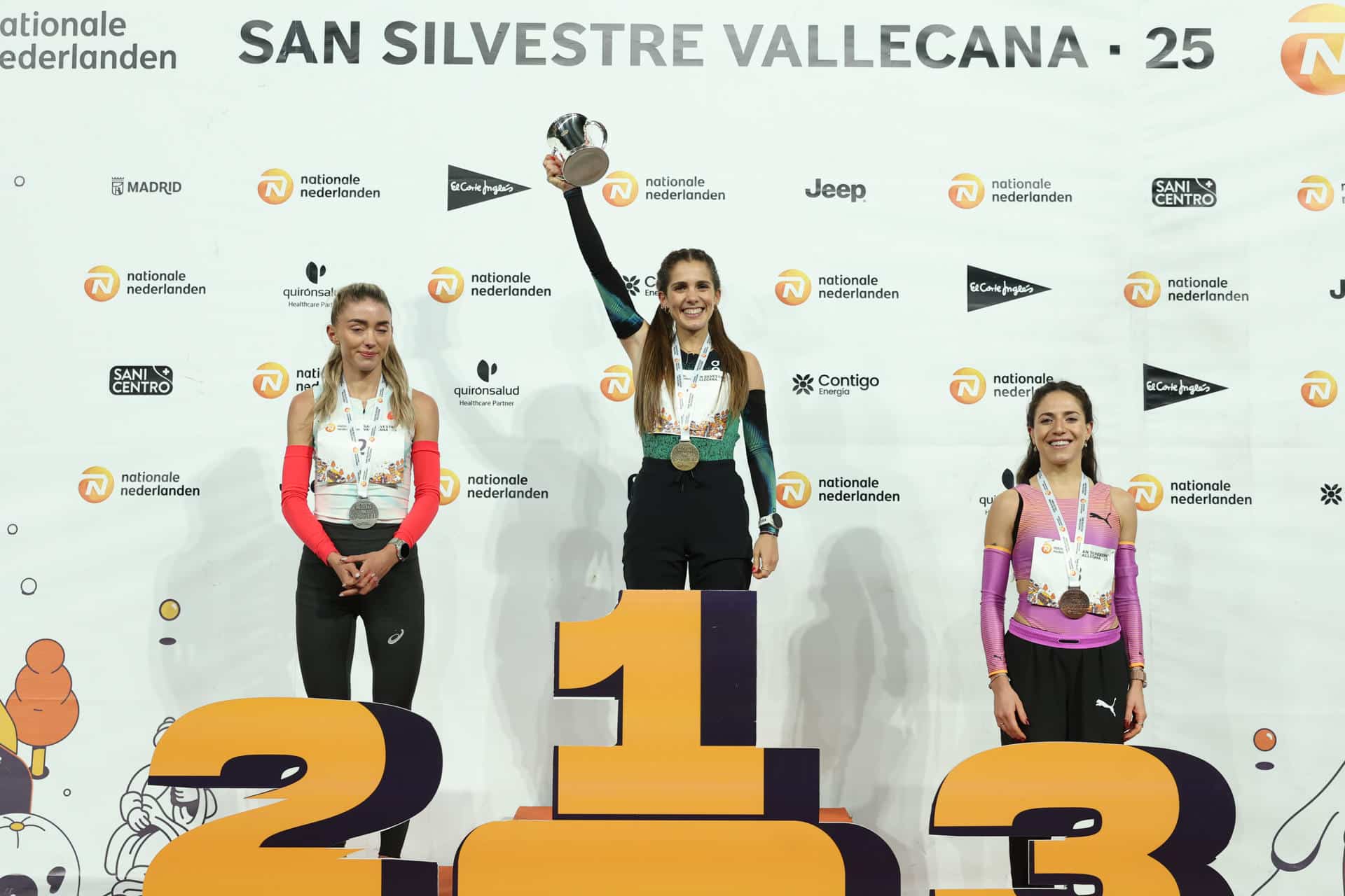 La atleta española Marta García (c) celebra en el podio su victoria junto a la segunda clasificada, la neerlandesa Diana van Es (i), y la tercera, la también española Carla Gallardo, en la prueba femenina internacional de la San Silvestre Vallecana, este miércoles en Madrid. EFE/Kiko Huesca