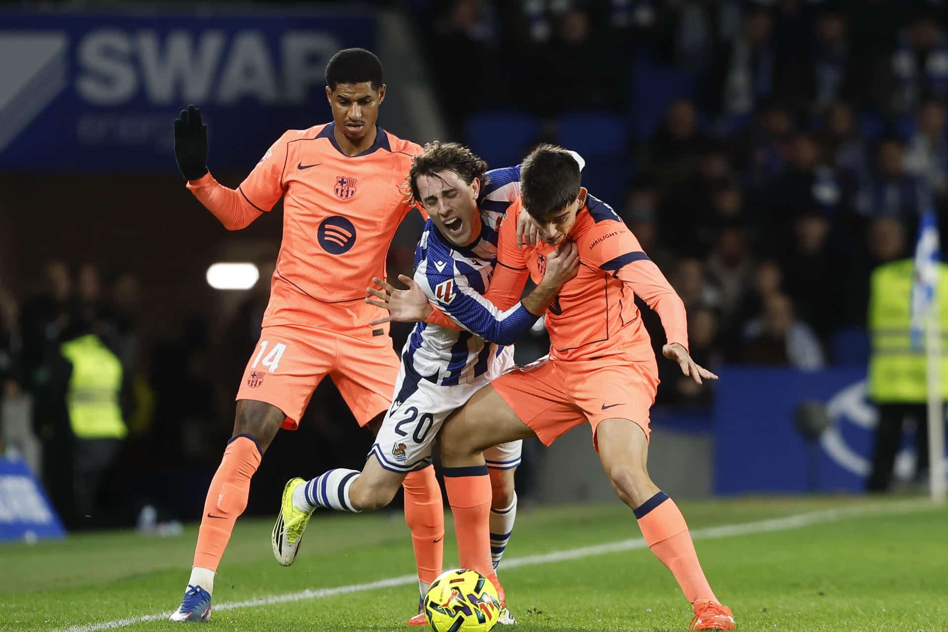 El defensa de la Real Álvaro Odriozola (c) cae entre Gerard Martín (d) y Marcus Rashford, ambos del Barcelona, durante el partido de LaLiga EA Sports que Real Sociedad y FC Barcelona han disputado en el estadio de Anoeta, en San Sebastián. EFE/Juan Herrero
