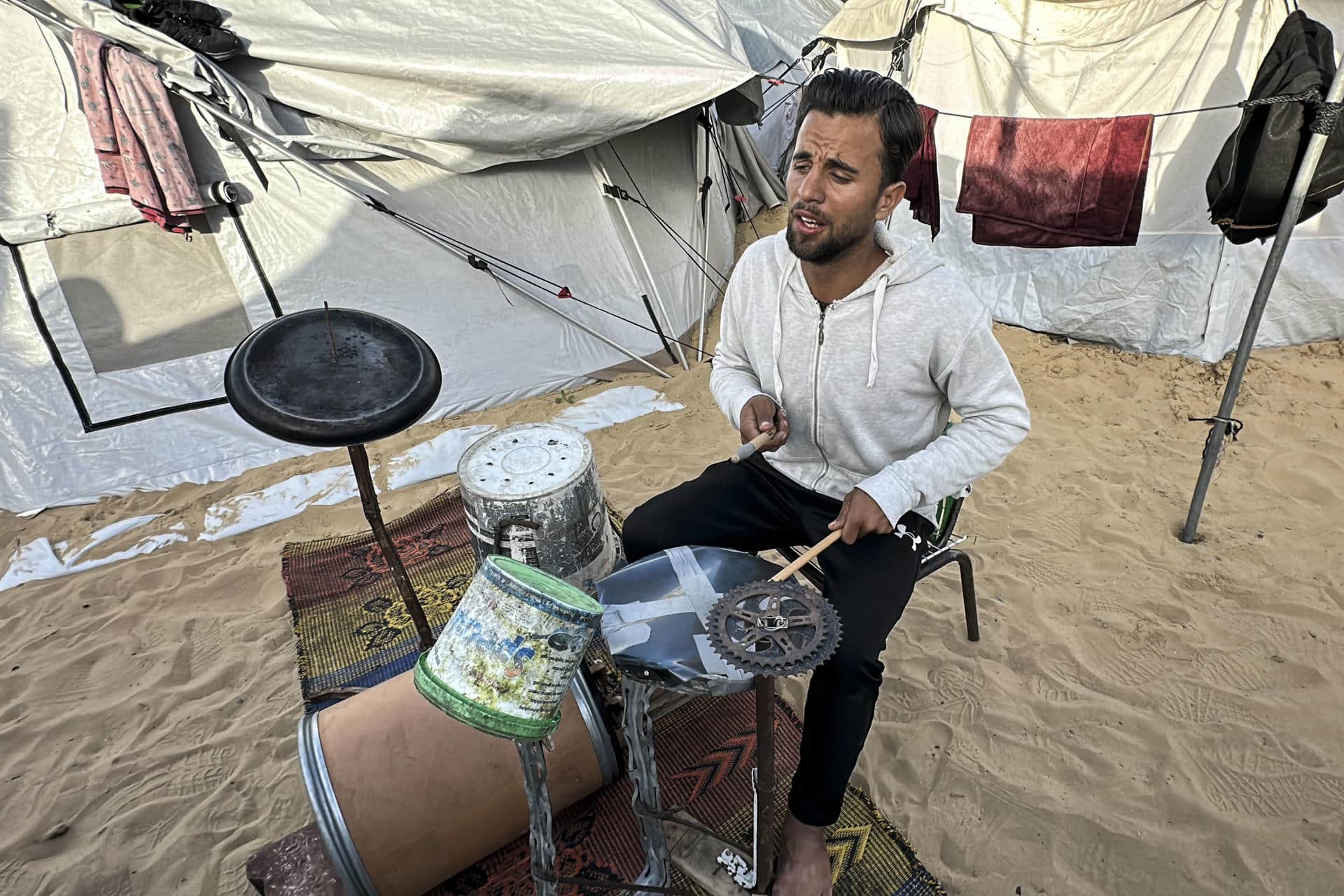 Con cajas de plástico, varas de metal, un barril y restos de una bicicleta el gazatí Hossam Qassem, de 24 años, desplazado en la zona costera de Mawasi (sur de la Franja), ha logrado construir una batería, un instrumento que le apasiona y que le sirve de terapia en medio de la desolación que persiste en el enclave palestino. "Cuando nos desplazaron, no pude llevarme el instrumento. Dejé de tocar durante mucho tiempo, por el hambre, la presión psicológica y la búsqueda diaria de comida y agua", explica a EFE este joven gazatí natural de Beit Lahia, en el norte de la Franja. EFE/